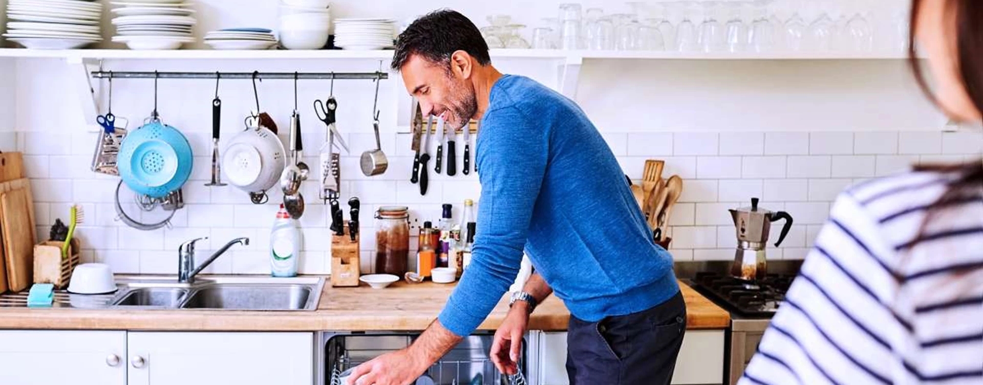 Man putting dirty coffee mugs into dishwasher in kitchen